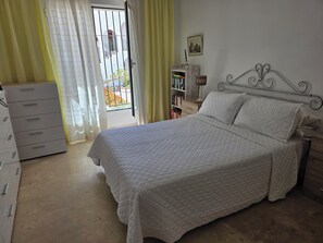 A bedroom with a bed, a dresser, a bookshelf, and a window with curtains. - A lovely spacious 2-bed apartment  on beautiful El Presidente Urbanisation, (Estepona)