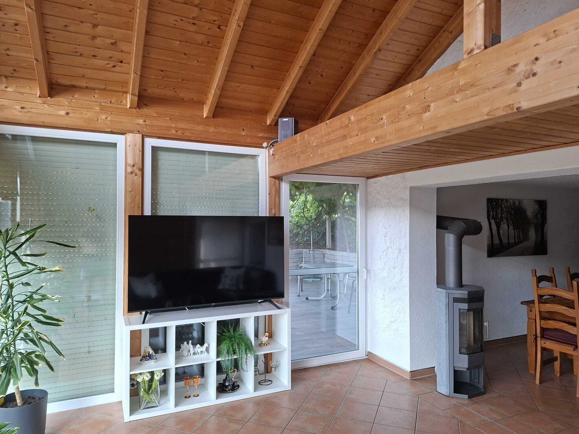 Ein modernes Wohnzimmer mit Flachbildfernseher, Holzbalkendecke, Glastür zu einer Außenpatio und einem Kamin.