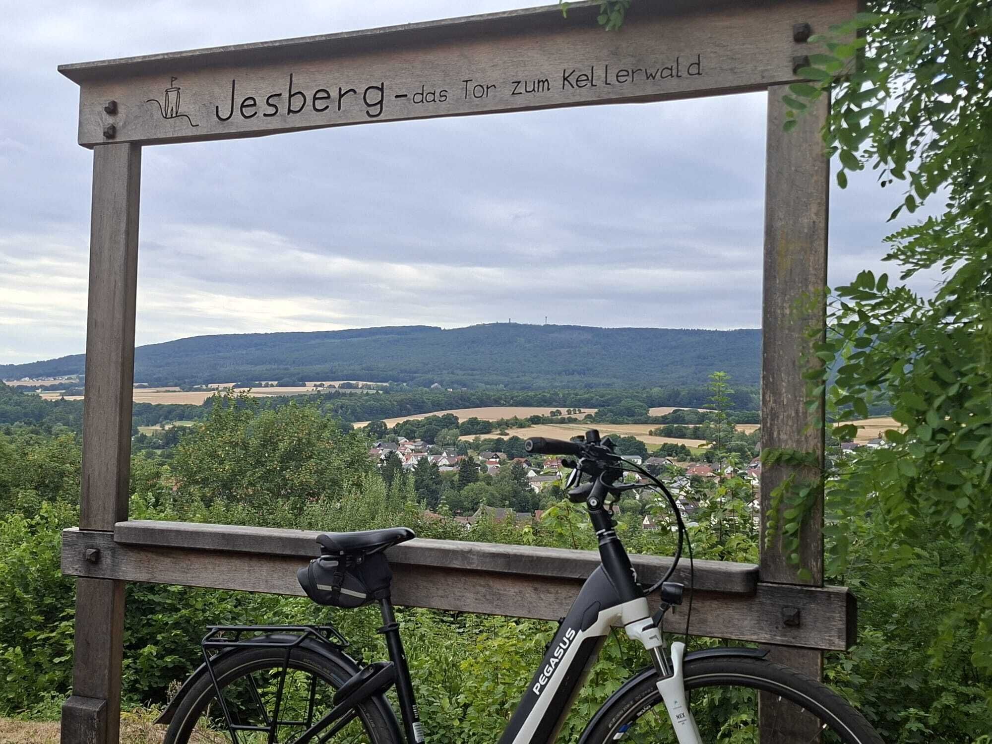 Ein Fahrrad vor einer Holzhütte mit Blick auf ein Tal und Hügel.