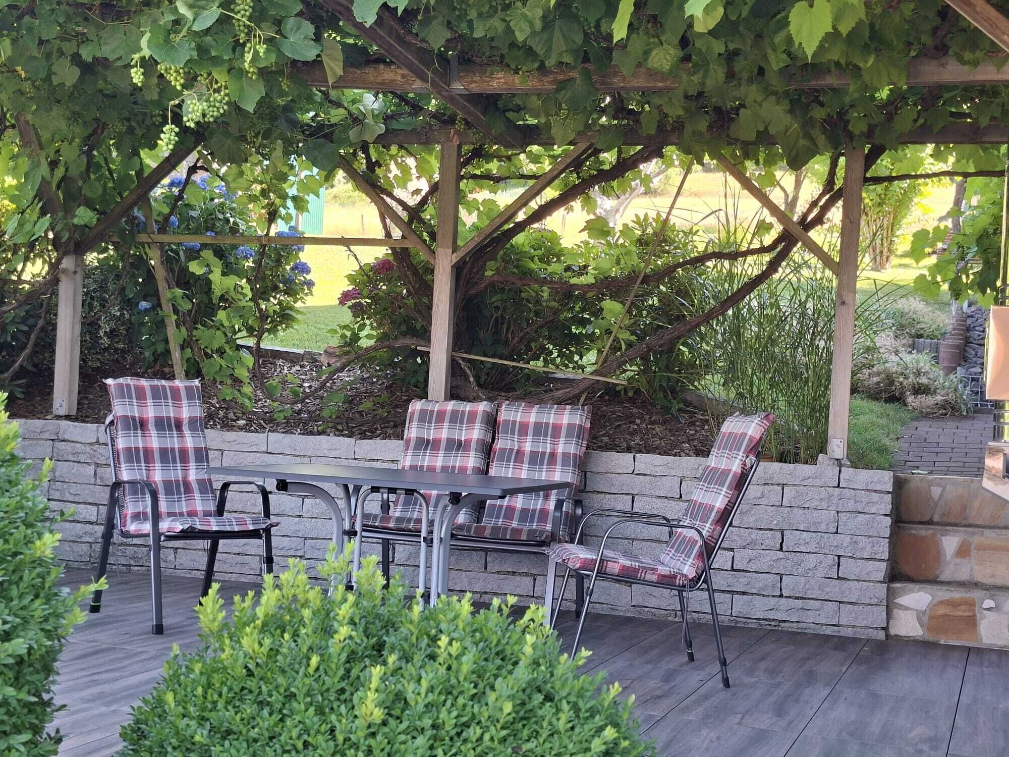 Eine Terrasse im Freien mit einer Pergola, einem Tisch und vier Stühlen mit Karokissen.