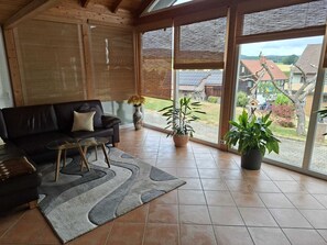 A spacious living area with a black sofa, a glass coffee table, and a grey rug. There are potted plants and a view of a residential area through large windows. - "Das Tor zum Kellerwald" Ferienwohnung mit privater Terasse und Wi-Fi (Jesberg)