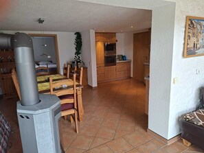 A cozy living area with a fireplace, wooden furniture, and a kitchen in the background. - "Das Tor zum Kellerwald" Ferienwohnung mit privater Terasse und Wi-Fi (Jesberg)