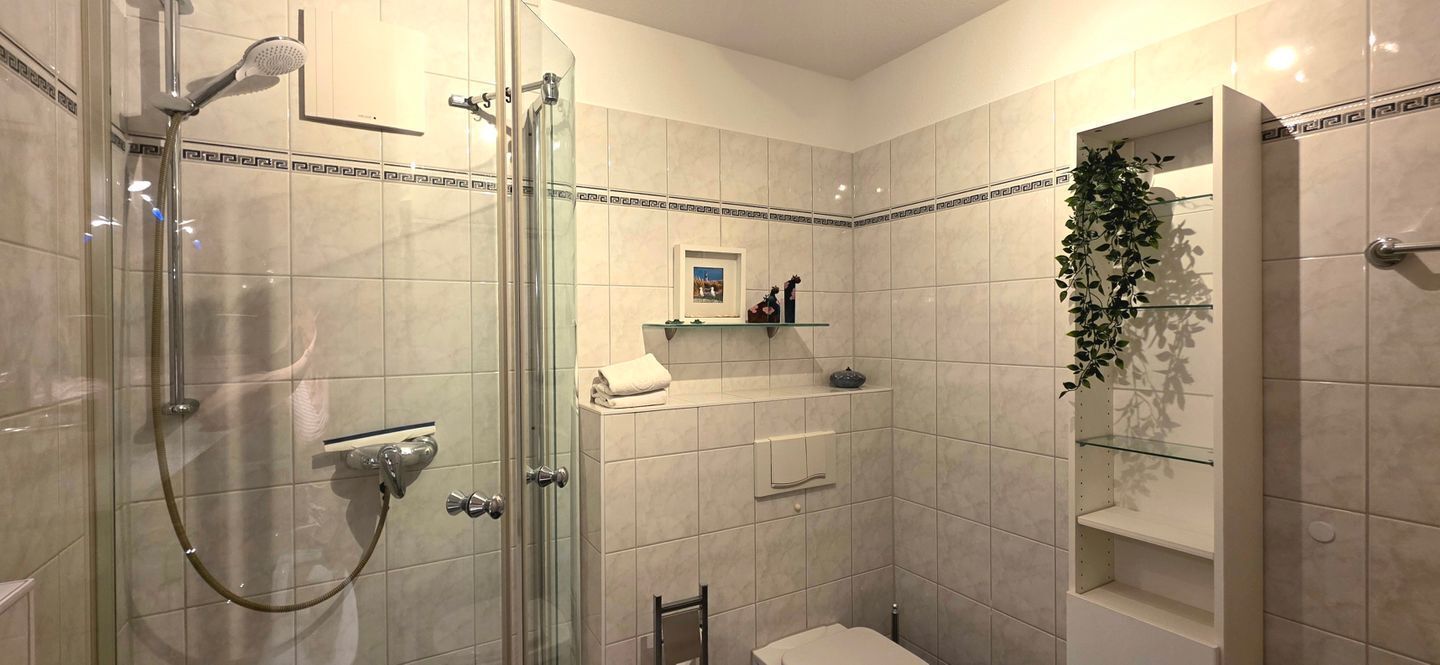 Une salle de bain moderne avec une douche à parois de verre, des toilettes et un lavabo surmonté d’une étagère en verre.