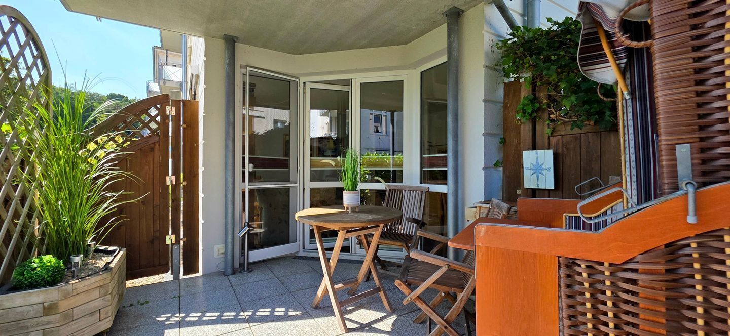 Un patio exterior con una mesa y sillas de madera, una valla de madera y una planta en maceta.