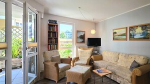 Un salon comprenant un canapé, deux fauteuils, une table basse, une bibliothèque, un téléviseur à écran plat et deux tableaux accrochés au mur.