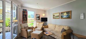 A living room with a sofa, two armchairs, a coffee table, a bookshelf, a flat-screen TV, and two paintings on the wall. - Vacation Rental i38 - Ground-floor 2-room apartment near the beach, Wi-Fi (Graal-Müritz)