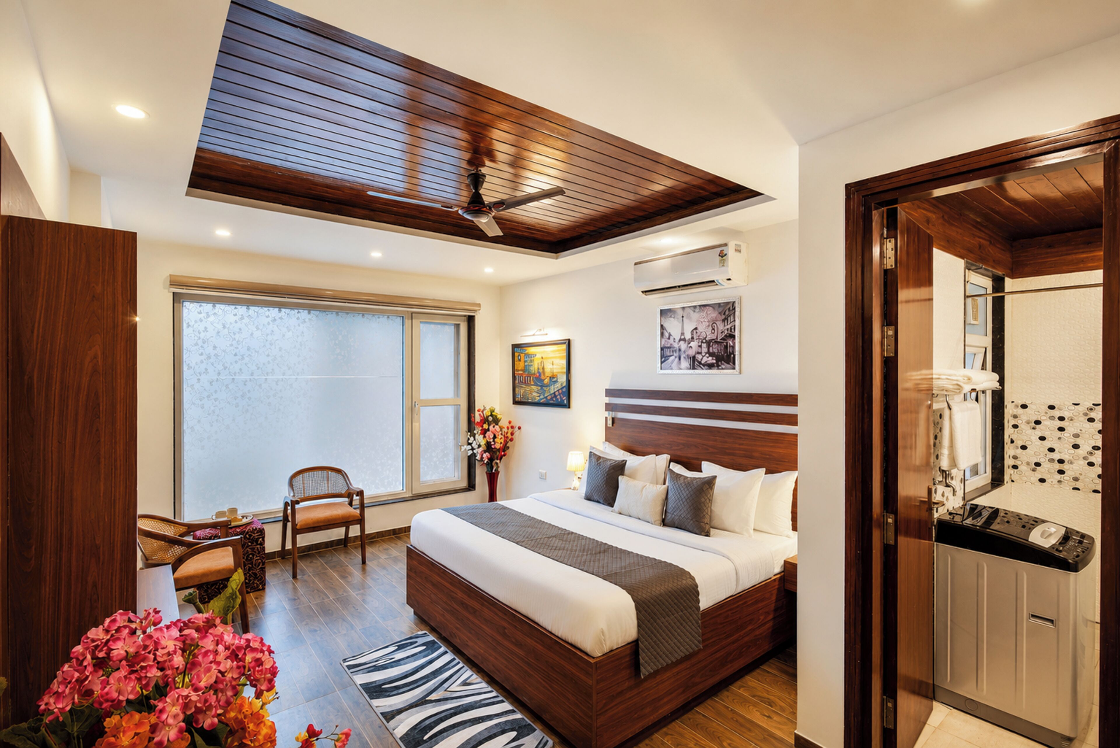 A modern bedroom with a large bed, a ceiling fan, a window with a view, and a bathroom with a shower and toilet.