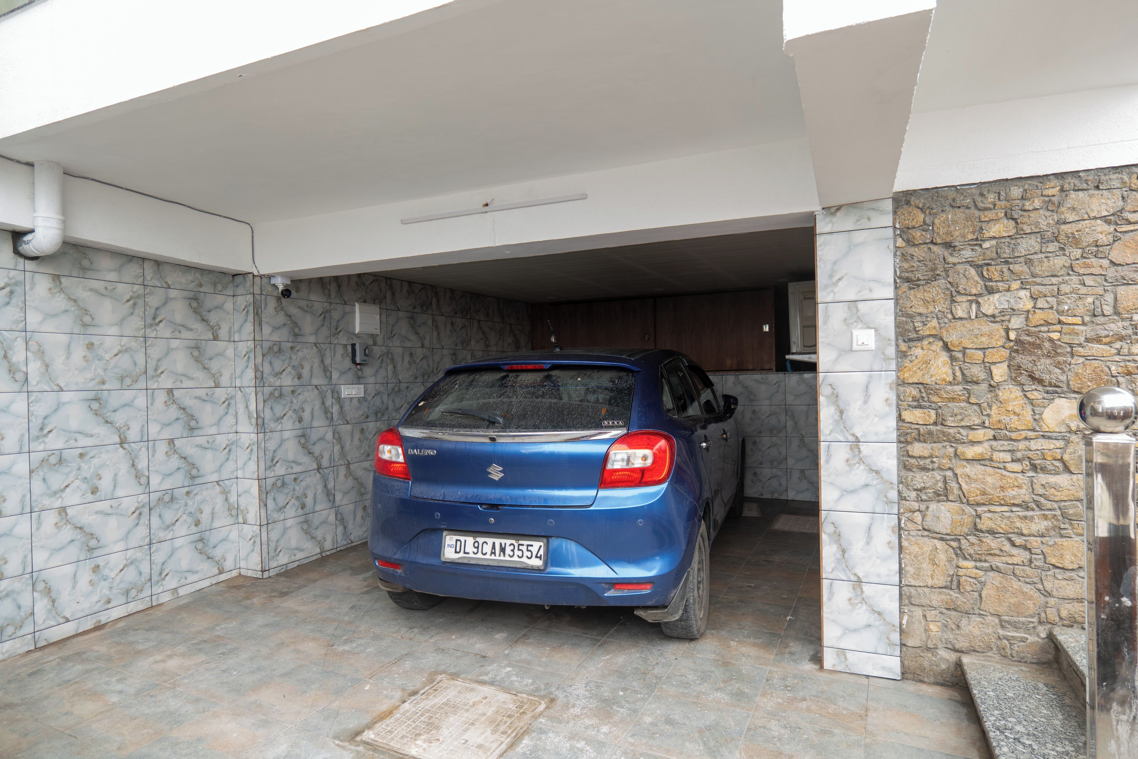 A blue car parked in a covered parking area with a stone wall and tiled floor.