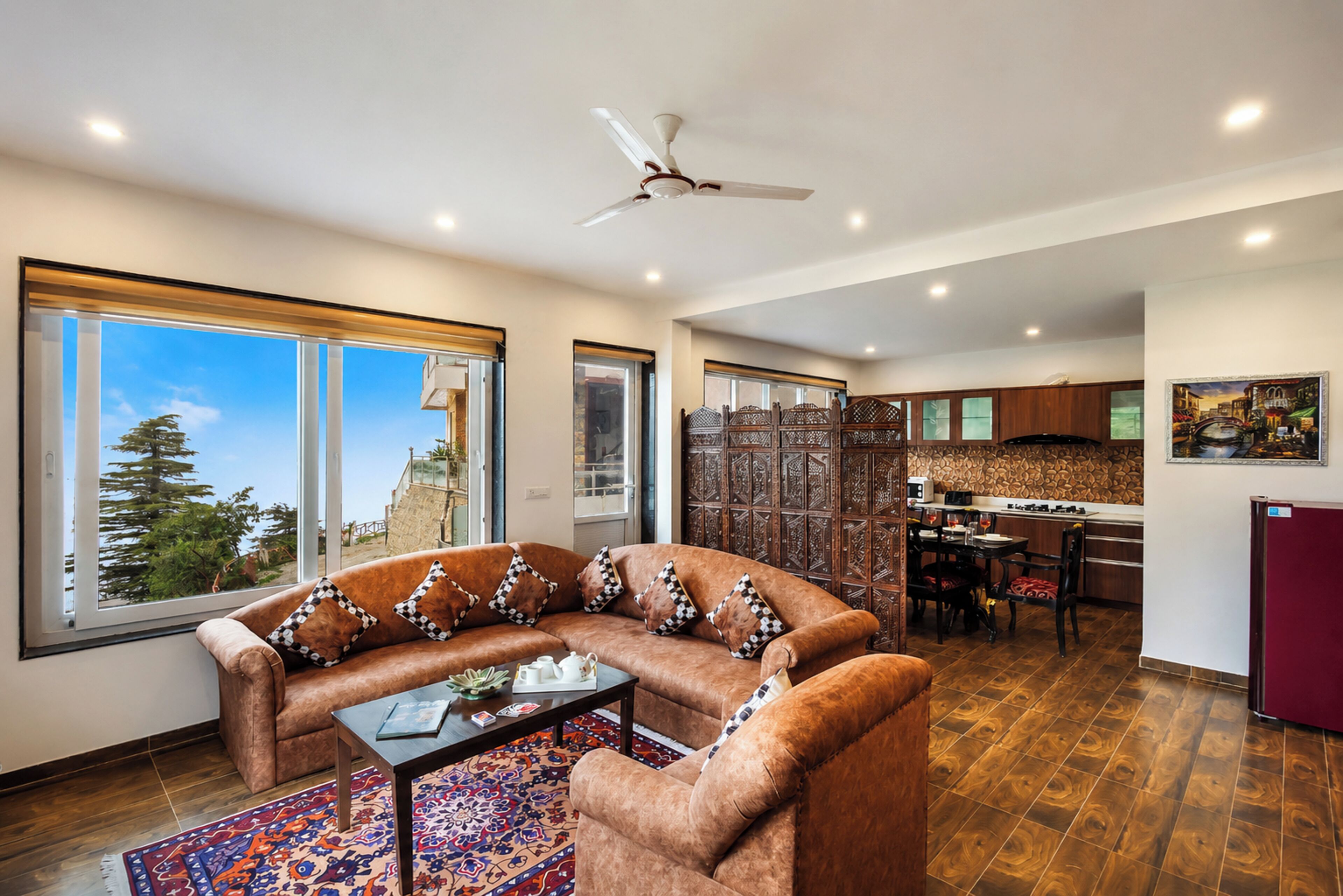 A living room with a sofa, a coffee table, and a view of a mountainous landscape through large windows.