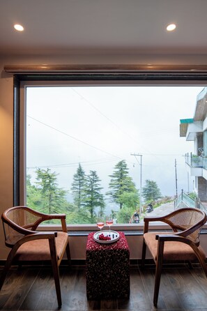 Ein Zimmer mit zwei Holzstühlen, die zu einem großen Fenster mit Blick auf eine gebirgige Landschaft zeigen.