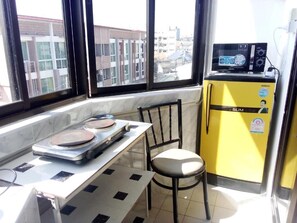 Una cocina pequeña con microondas, un refrigerador amarillo, una mesa con una silla y una ventana con vista a la ciudad.