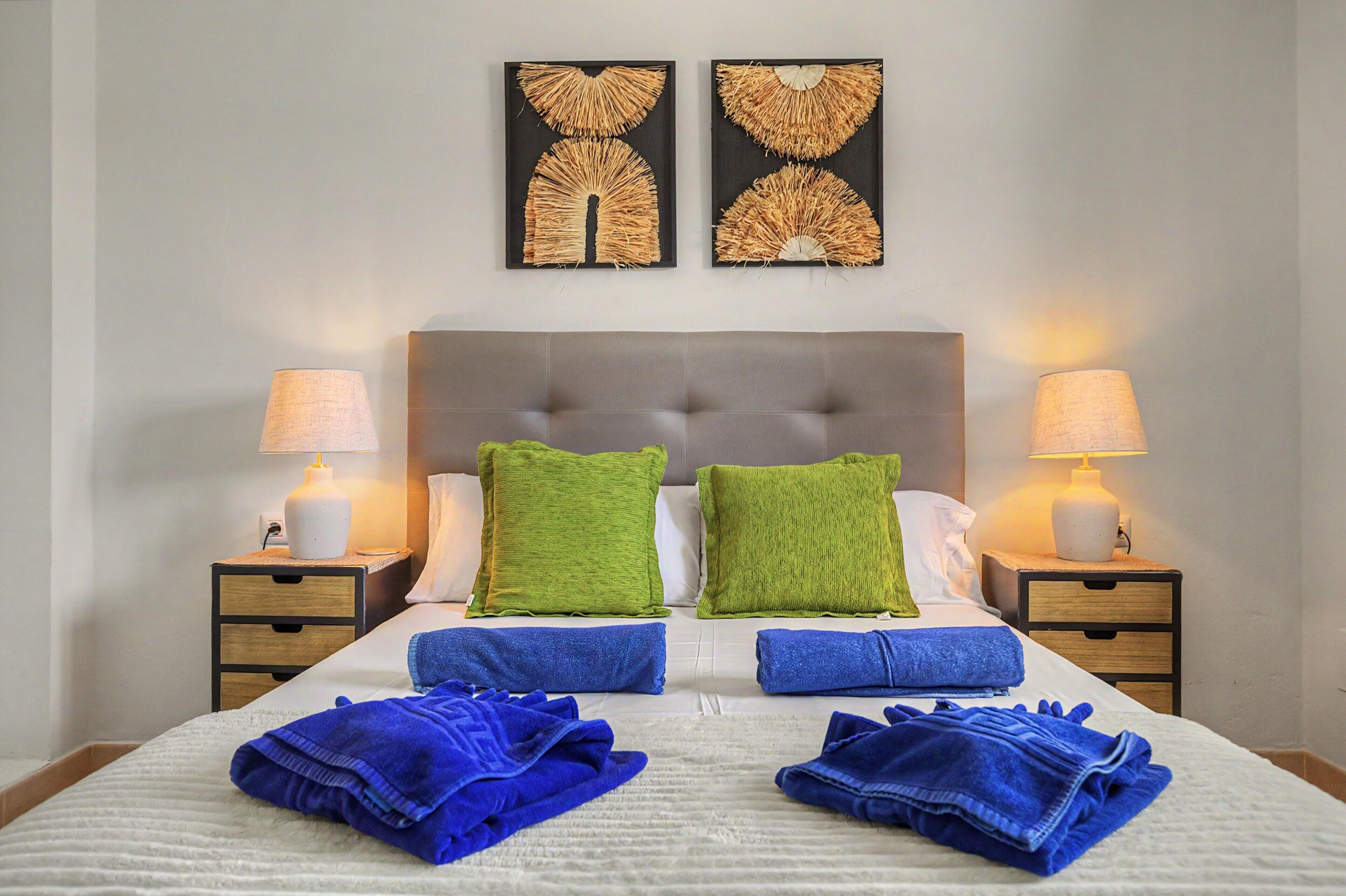 Une chambre d’hôtel avec un lit, deux tables de chevet, deux lampes, deux coussins verts et deux serviettes bleues.