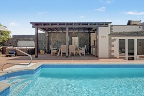 A swimming pool with a covered patio area, stone walls, and outdoor furniture. - Vacation Villa 'Eire' with Mountain View, Wi-Fi and Air Conditioning (Yaiza)