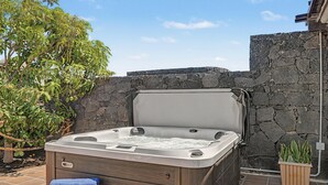Un bain à remous avec une structure extérieure en bois, placé contre un mur de pierre, et agrémenté d’une plante en pot à proximité.