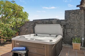 Ein Whirlpool mit Holzverkleidung, platziert an einer Steinwand, mit einem Blumentopf in der Nähe.