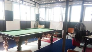 Een pooltafel in een ruimte met grote ramen, een ventilator en een stoel.