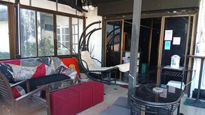 Een kamer met een bank, een rode poef, een glazen tafel en een stoel. Er is een trap die naar een ander niveau leidt.