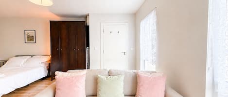 A bedroom with a bed, a sofa with cushions, a wardrobe, a door, and a window with curtains.