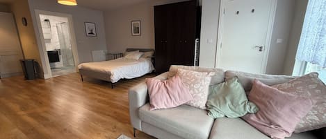 A spacious living area with a sofa, a bed, and a dining table. There are two pendant lights hanging from the ceiling.