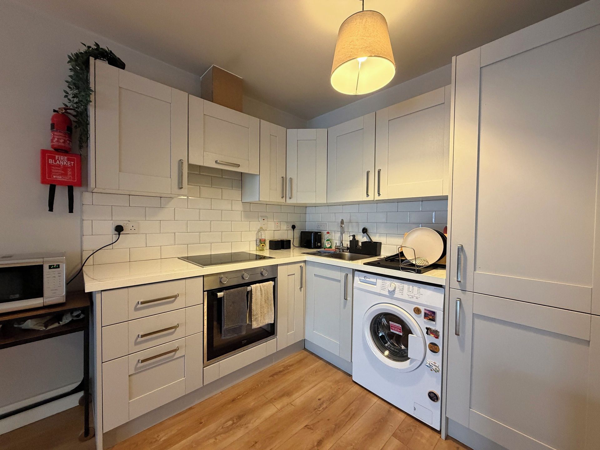 Cocina moderna con alacenas blancas, microondas, horno, lavadora y una lámpara colgante.
