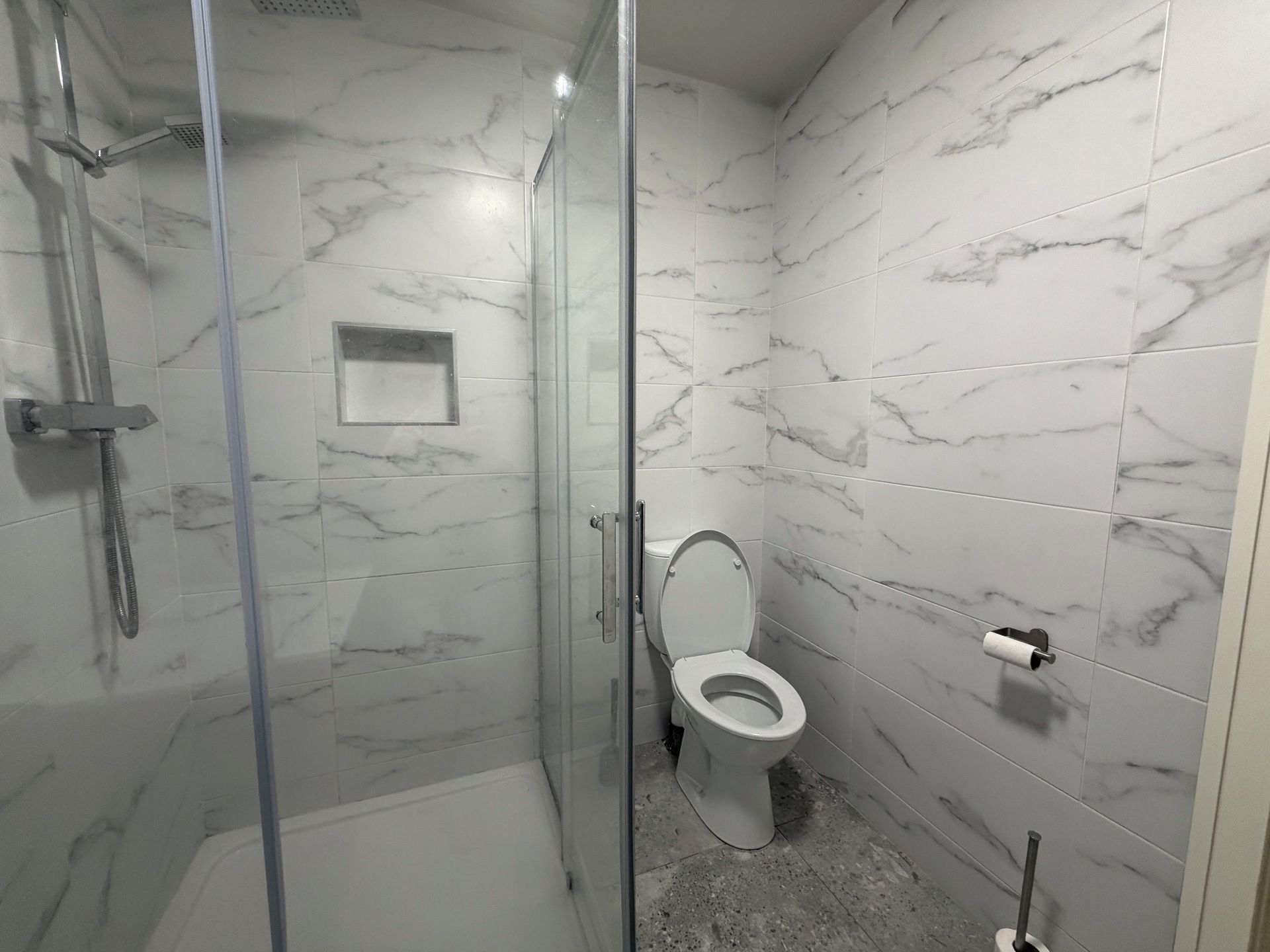 A bathroom with a glass-enclosed shower, a toilet, and marble-patterned walls.
