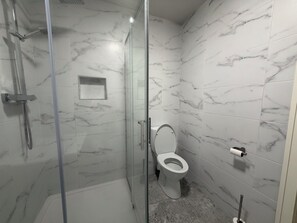 A bathroom with a glass-enclosed shower, a toilet, and marble-patterned walls.