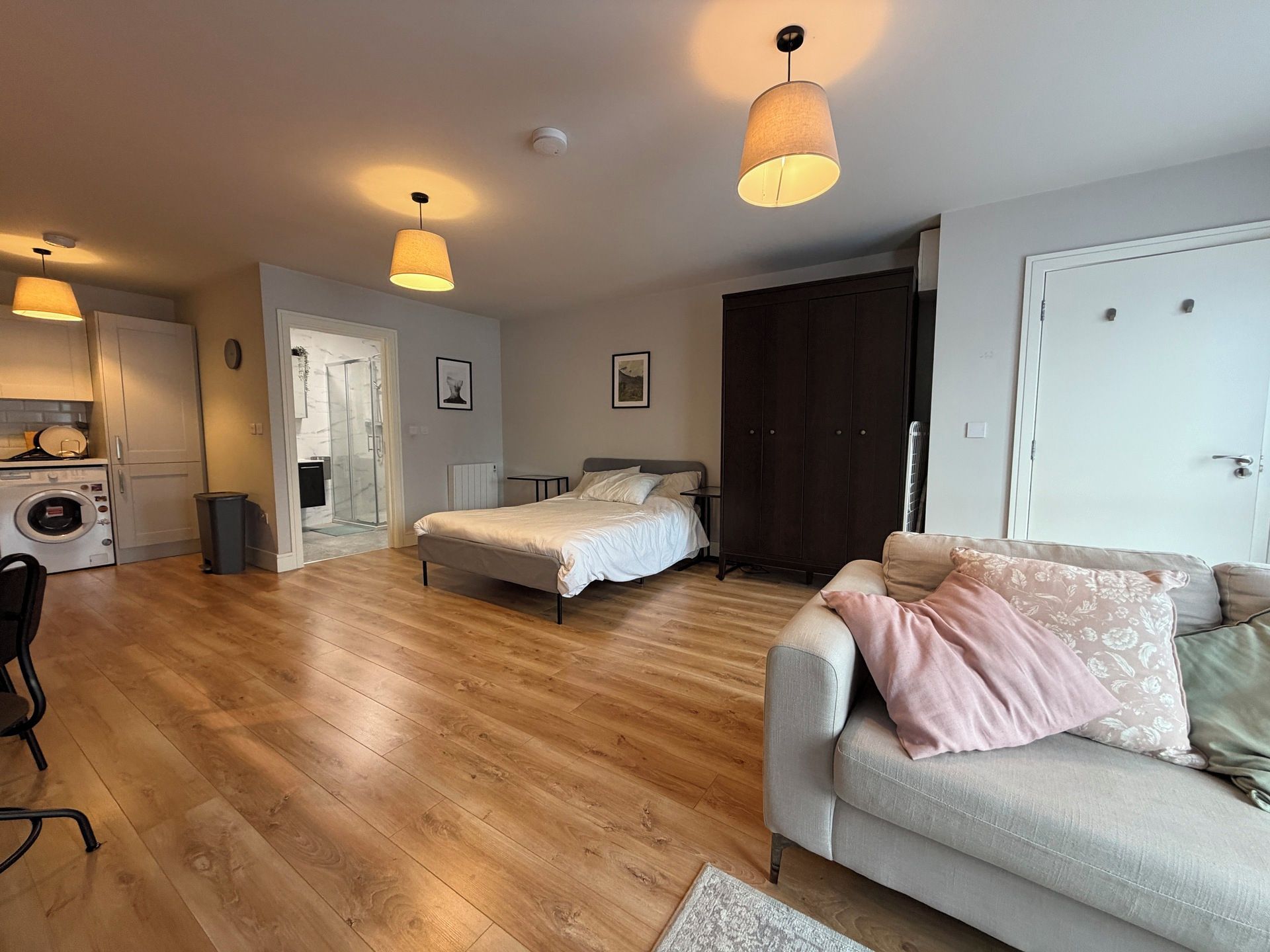 Amplia sala de estar con sofá, cama y mesa de comedor. Cuenta con una zona de cocina con lavadora y refrigerador.