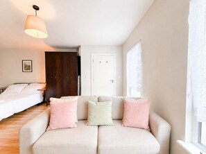 A bedroom with a bed, a sofa with cushions, a wardrobe, a door, and a window with curtains.