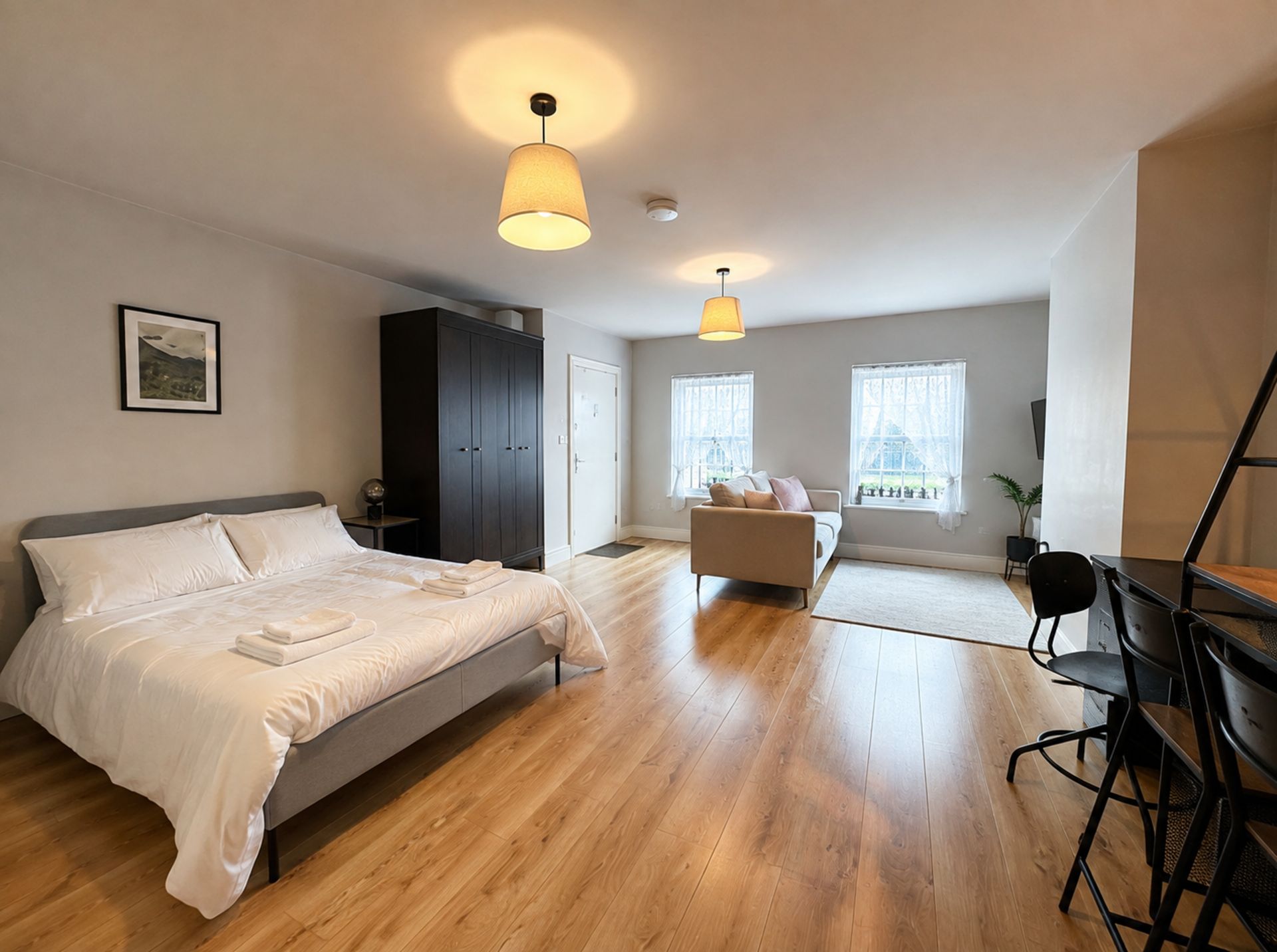 Un dormitorio moderno con una cama grande, un armario oscuro, un escritorio con una silla y una ventana con vistas.