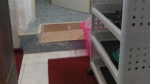 Un baño con ducha, una puerta blanca, un estante blanco y un tapete rojo.