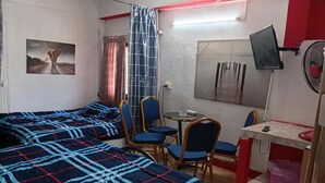 Una habitación con dos camas, una mesita, sillas, un televisor y un ventilador.
