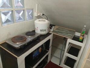 Una kitchenette compacta con estufa a gas, una cocedora de arroz y una pequeña mesa con una botella.