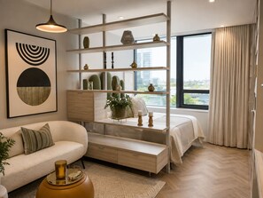 A modern living room with a sofa, a coffee table, a bookshelf, and a large window with a view of buildings. - Tranquil Foreshore Studio Fully Equipped & Central (Cape Town)