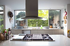 A modern kitchen with a central island, a large window, and a view of greenery outside.