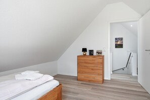 A bedroom with a bed, a wooden dresser, and a door leading to a bathroom. - Ebbe&Flut - Modern Ebbe&Flut Vacation Rental in Norddeich for the Whole Family (Norden)