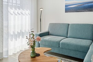 A living room with a sofa, a round wooden coffee table, and a vase with flowers. - Ebbe&Flut - Modern Ebbe&Flut Vacation Rental in Norddeich for the Whole Family (Norden)