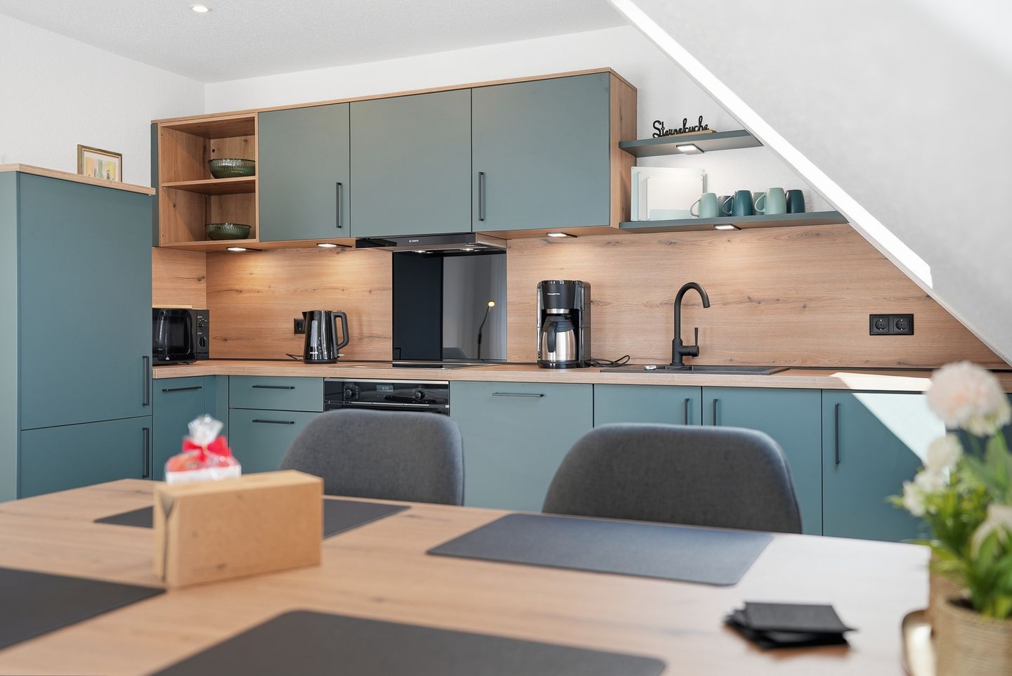 A modern kitchen with teal cabinets, a wooden countertop, a coffee maker, and a sink.