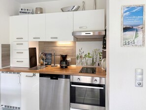 A modern kitchen with white cabinets, a coffee maker, and a view of the beach. - House at Badeweg 4 - "Sandkorn 1" Apartment (Scharbeutz)