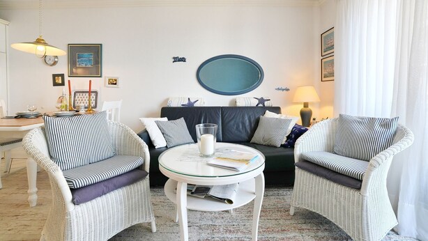 A room with a round glass table, two wicker chairs, a sofa, and a wall-mounted round mirror. - Seebrücke Apartment 11 - Seebrücke (Scharbeutz)