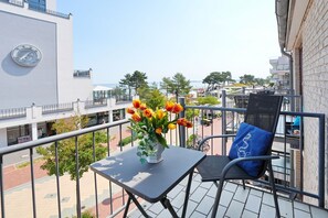 Ein Balkon mit Tisch, Stuhl und Blumen in einer Vase.