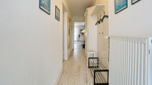 A hallway with framed artwork on the walls, a radiator, and a small table with a chair. - Seebrücke Apartment 11 - Seebrücke (Scharbeutz)