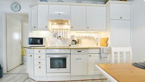 A kitchen with white cabinetry, a microwave, an oven, a dishwasher, and a clock on the wall. - Seebrücke Apartment 11 - Seebrücke (Scharbeutz)