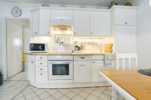 Eine Küche mit weißen Schränken, einer Mikrowelle, einem Backofen, einem Geschirrspüler und einer Uhr an der Wand.