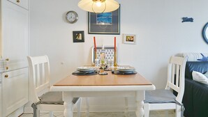 A dining area with a wooden table, white chairs, a clock, and framed pictures on the wall. - Seebrücke Apartment 11 - Seebrücke (Scharbeutz)
