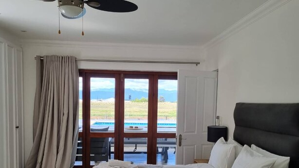 A bedroom with a bed, a ceiling fan, a view of a pool and mountains through a glass door. - Country Retreat with Pool & Braai, Sleeps 6 (Riebeek-Kasteel)