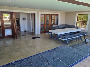 Un espace piscine intérieur avec une table et des bancs, une porte donnant sur l’extérieur et une vue à travers les portes vitrées.