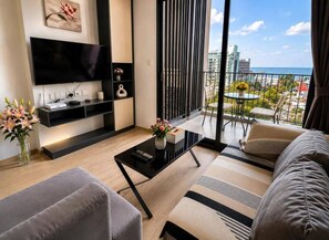En moderne stue med et fladskærms-tv, et sofabord, en sofa og en balkon med udsigt over byen og havet.