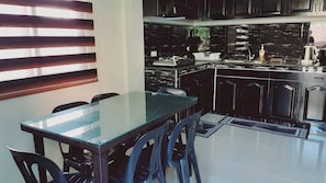A modern kitchen with black cabinets, a glass dining table, and a black countertop. - Avana Hills Boracay Prime - Grand (Malay)