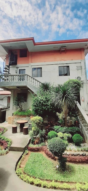 A two-story building with a balcony, a staircase leading to the upper floor, and a well-maintained garden with various plants and shrubs. - Avana Hills Boracay Prime - Grand (Malay)