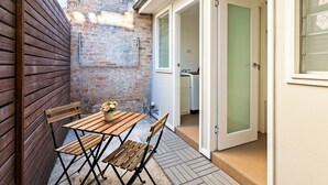 Eine kleine Terrasse mit Holztisch und -stühlen, einer Ziegelwand und einer Tür zu einem Zimmer.